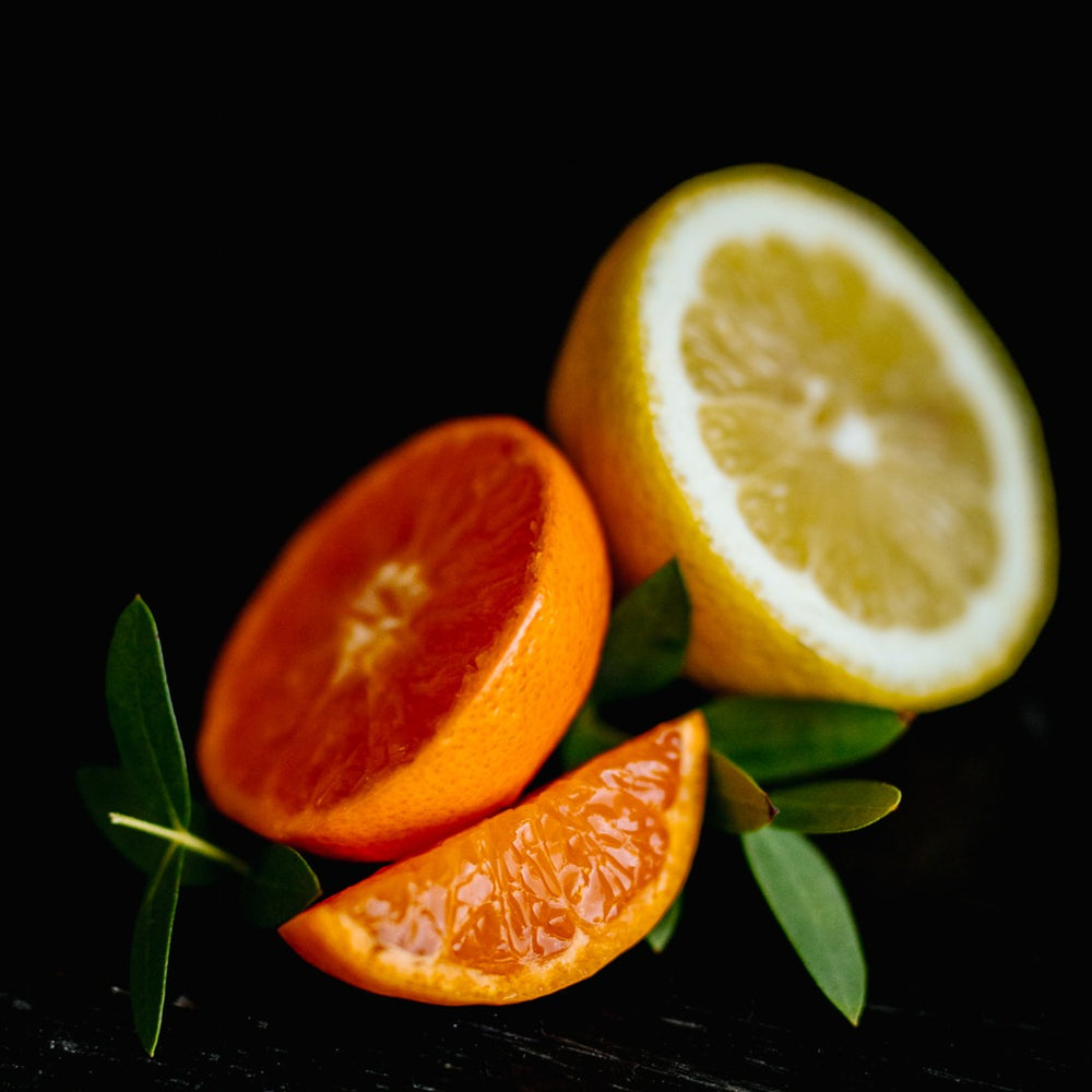 Close-up of sliced citrus fruits including an orange and lemon with green leaves on black background