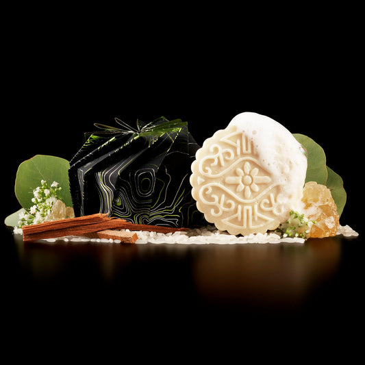 EPS bee hive styled shampoo bar with foam, cinnamon sticks, crystals, white flowers, and green leaves on black
