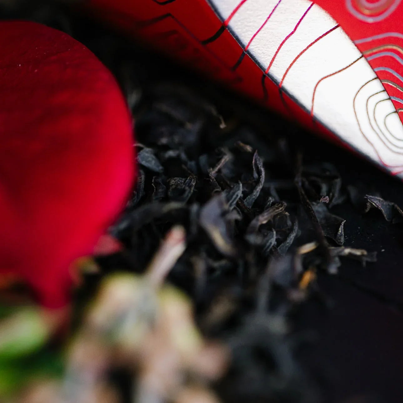 Close-up of loose black tea leaves with red and white patterned packaging in background