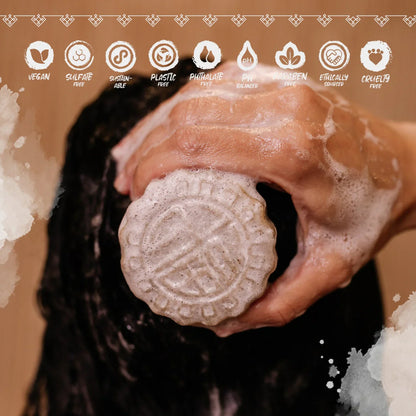 Hand holding a foaming eps bee hive shampoo bar on wet black hair with vegan and sulfate-free icons