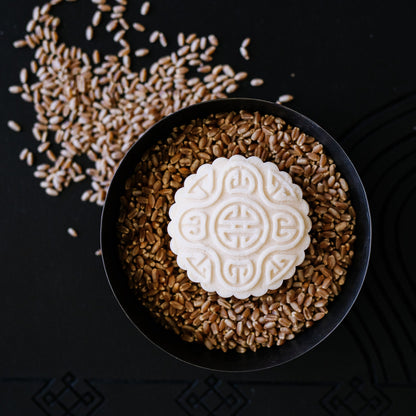 Decorative white mooncake with intricate pattern on a bowl of wheat grains on black background