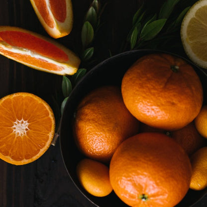 assorted fresh citrus fruits including oranges, kumquats, and grapefruit on a dark surface with green leaves