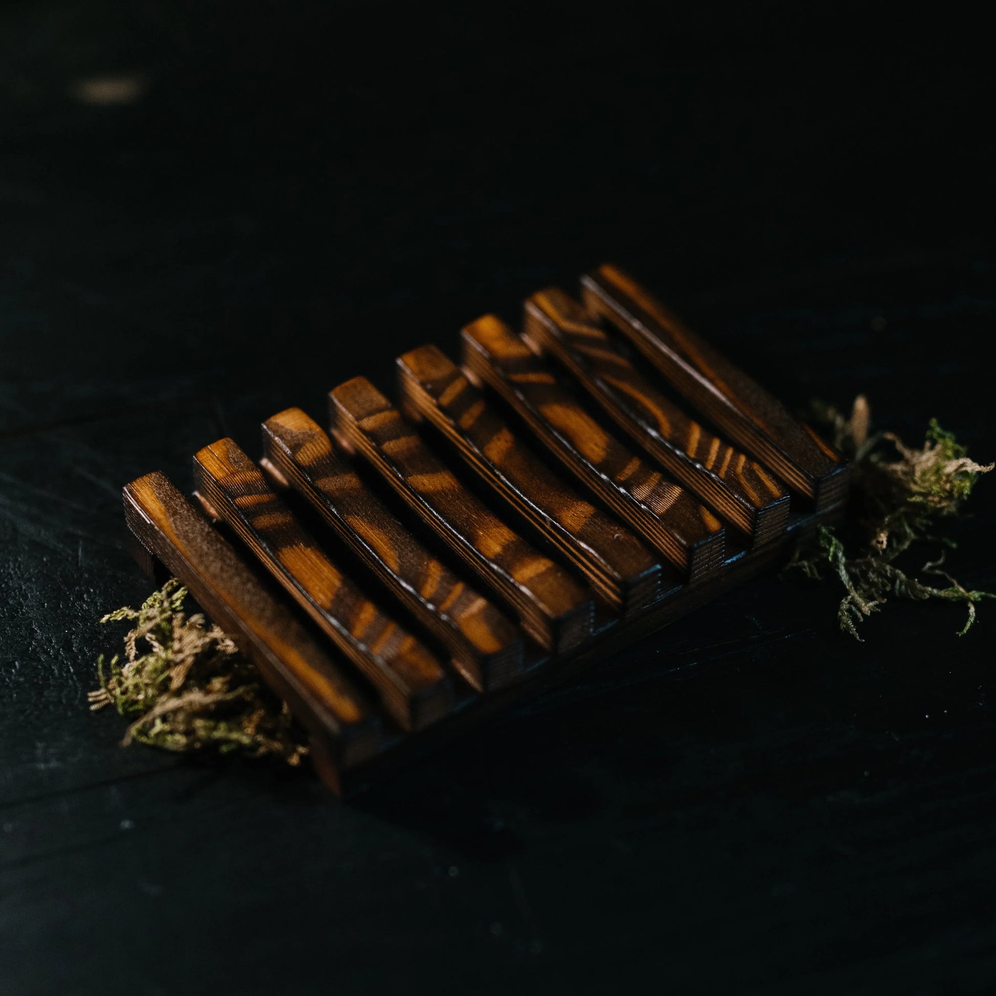 Close-up of a dark wood EPS bee hive frame with distinctive grain, placed on dark surface with moss